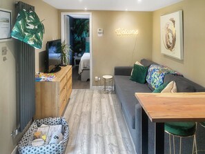 Ein modernes Wohnzimmer mit einer Couch, einem Holztisch, einem Haustierbett, einem Fernseher und einem 'Welcome'-Schild.