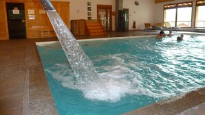 En inomhuspool med en vattenfontän, träväggar och ett kaklat golv.