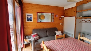 Ett mysigt rum med en väggpanel av trä, en grå soffa, ett litet bord med en rutig duk och en spegel ovanför soffan.