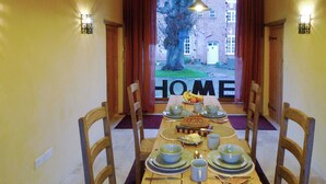 Une table à manger dressée pour quatre personnes, avec des chaises en bois, un pain et un saladier de fruits posés sur la table.