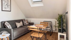 A cozy living room with a grey sofa, a wooden dining table, and a small white table. - 2 bedroom accommodation in West Mersea (West Mersea)