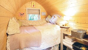 A cozy wooden cabin bedroom with a bed, pillows, a window with a view, and a shelf with towels. - 1 bedroom accommodation in Woolton Hill, nr Newbury (Woolton Hill, nr Newbury)
