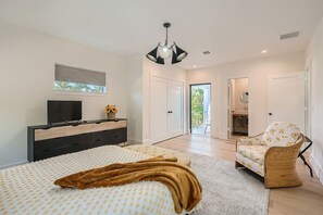 Un dormitorio moderno con cama, cómoda, televisor y una silla.