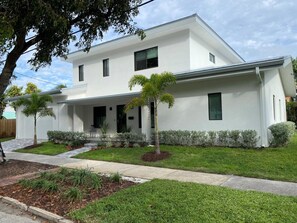 Una casa moderna de dos pisos con un porche cubierto, un césped cuidado y un árbol pequeño.