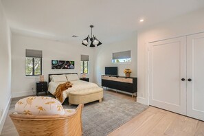 Un dormitorio con cama, mesitas de noche, cómoda, televisor y una puerta.