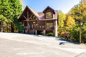 A wooden lodge with a stone foundation, a porch, and a large window. - 3BR Cabin: Hot Tub, Game Room, Near Strip, Porches (Pigeon Forge)