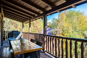 A wooden deck with a table and chairs, overlooking a forested area with autumn foliage. - 3BR Cabin: Hot Tub, Game Room, Near Strip, Porches (Pigeon Forge)