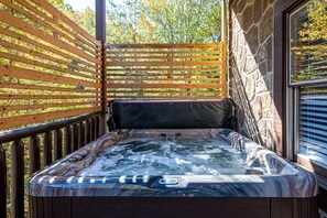 A hot tub with a wooden deck and stone wall, surrounded by a wooden fence. - 3BR Cabin: Hot Tub, Game Room, Near Strip, Porches (Pigeon Forge)