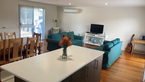 Een moderne woonkamer met een eethoek, saladesoap in teal-kleur, een televisie en een gitaar.