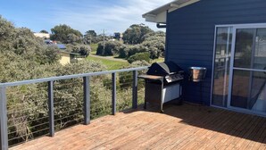 Een balkon met een barbecue en een kruidenrek, met uitzicht op een tuin en een weg.