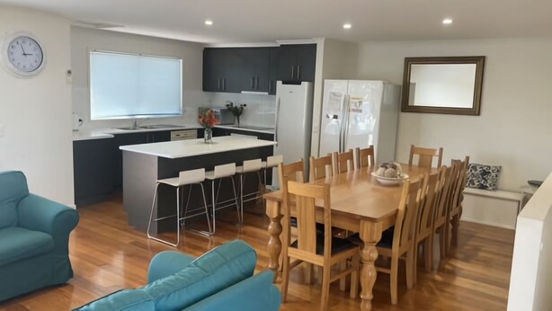 Een moderne keuken met donkere kastjes, een wit aanrechtblad en een ingebouwde oven. Er is een zithoek met een houten tafel en stoelen, en een blauwe bank in de woonkamer.