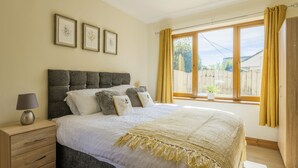 A bedroom with a large bed, a bedside table with a lamp, and a window with curtains. - Stunning 5-Bedroom Home in Truro (Truro)