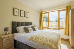 A bedroom with a large bed, a bedside table with a lamp, and a window with curtains. - Stunning 5-Bedroom Home in Truro (Truro)