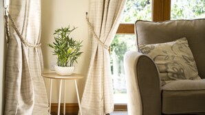 A cozy room with a sofa, a small table with a potted plant, and curtains drawn to one side. - Stunning 5-Bedroom Home in Truro (Truro)