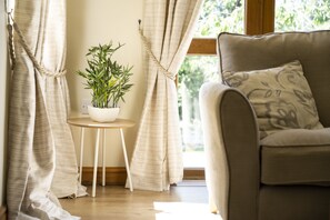 A cozy room with a sofa, a small table with a potted plant, and curtains drawn to one side. - Stunning 5-Bedroom Home in Truro (Truro)
