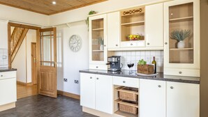 A modern kitchen with white cabinets, a wooden staircase, a clock, and a coffee machine. - Stunning 5-Bedroom Home in Truro (Truro)