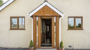A building with a wooden entrance, two potted plants, and a small window on the side. - Stunning 5-Bedroom Home in Truro (Truro)