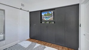 Une chambre à coucher avec un lit, une armoire grise et un écran de télévision qui diffuse une vue sur la piscine.