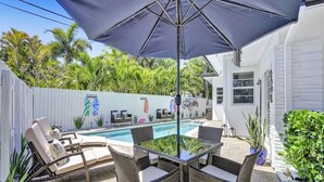 Un jardin avec une piscine, des meubles en osier et une clôture blanche agrémentée de décorations colorées.