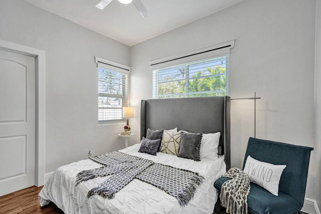 Un dormitorio con cama, mesitas de noche, una silla y ventanas.