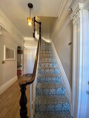 A staircase with patterned carpet, a wooden handrail, and a light fixture.