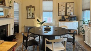 A dining area with a round table, chairs, a chandelier, a fireplace, and a kitchen in the background. - Townhouse Apt 2 w Parking in Downtown Portsmouth (Portsmouth)