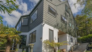 Une maison moderne avec un toit en pente, de grandes fenêtres et un escalier en bois menant à l’entrée.
