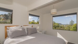 Une chambre à coucher avec un grand lit, deux fenêtres donnant sur un beau paysage, une table de chevet et un luminaire suspendu.