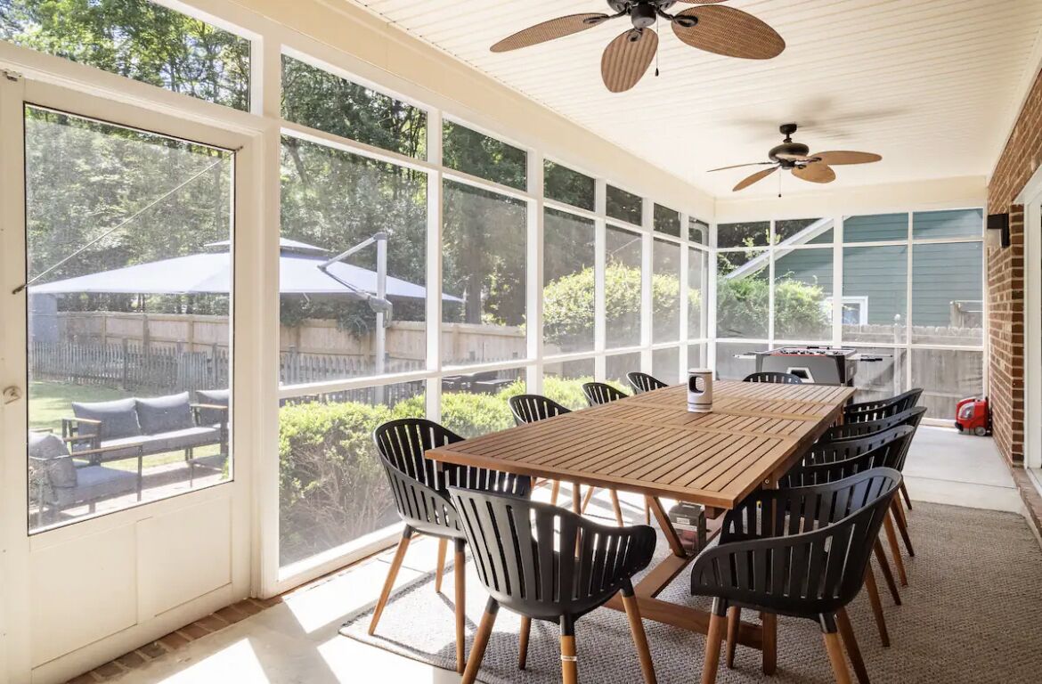 A sunroom with a large table and chairs, a ceiling fan, and large windows offering a view of the backyard.