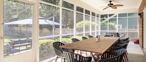 A sunroom with a large table and chairs, a ceiling fan, and large windows offering a view of the backyard.