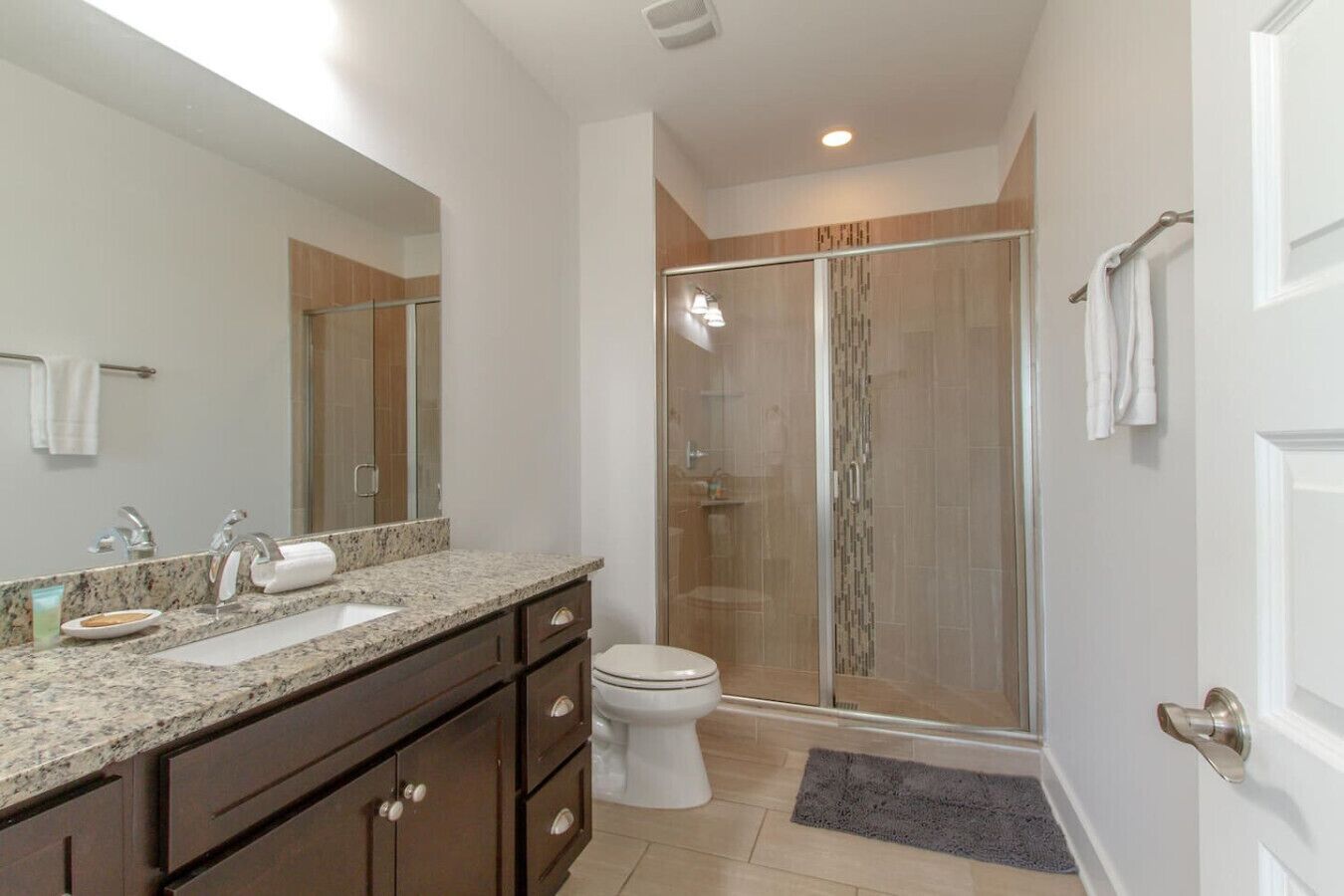 Une salle de bain moderne dotée d’un meuble-lavabo à deux vasques, de toilettes et d’une douche à parois de verre.