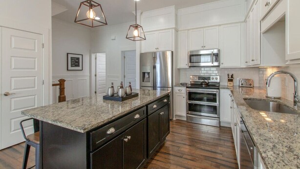A modern kitchen with white cabinets, granite countertops, stainless steel appliances, and pendant lighting. - Modern Luxury | Spacious Comfort | Prime Location (Nashville)