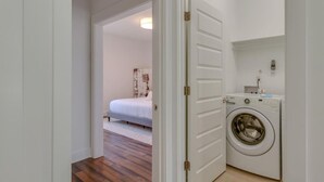 A bedroom with a bed, a washing machine, and a door leading to another room. - Modern Luxury | Spacious Comfort | Prime Location (Nashville)