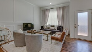 A modern living room with a sofa, two armchairs, a coffee table, a TV, and a large window with curtains. - Modern Luxury | Spacious Comfort | Prime Location (Nashville)