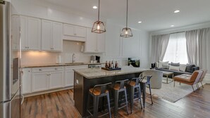 A modern kitchen with white cabinets, a central island with bar stools, and pendant lighting. - Modern Luxury | Spacious Comfort | Prime Location (Nashville)