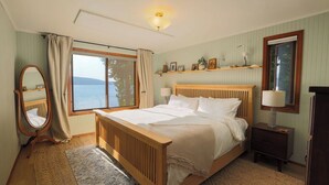 A bedroom with a large bed, a bedside table, a mirror, and a window with a view of the sea. - Private Waterfront Spa Retreat + Movie Theater (Port Townsend)