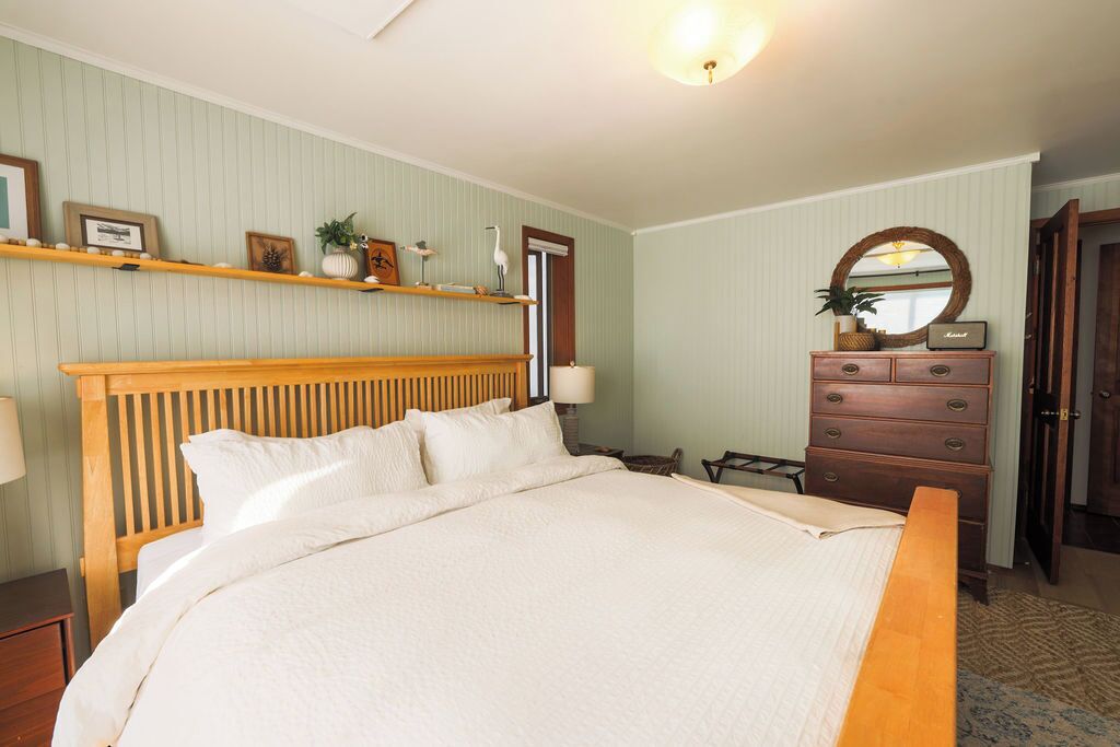 A bedroom with a large bed, wooden headboard, a dresser, a mirror, and shelves with decorative items.