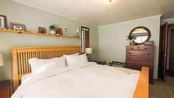 A bedroom with a large bed, wooden headboard, a dresser, a mirror, and shelves with decorative items.