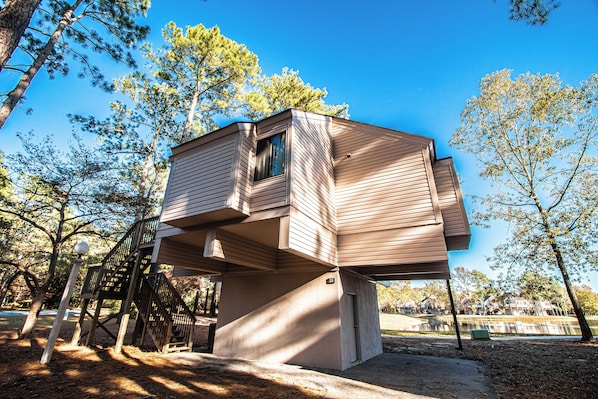 A unique treehouse structure with a small window and a staircase leading up to it, surrounded by trees and a clear sky.