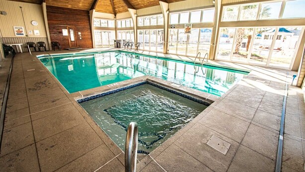Ein Hallenbad mit Fliesenboden, Sprungbrett und Holzbalkendecke.