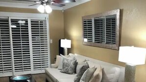 Ein Wohnzimmer mit beiger Couch, einem gemusterten Teppich und einem Deckenventilator.