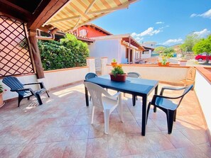 An outdoor patio with a table and chairs, a potted plant, and a view of the surrounding neighborhood. - I Geranei 2 San Teodoro Centro (San Teodoro)