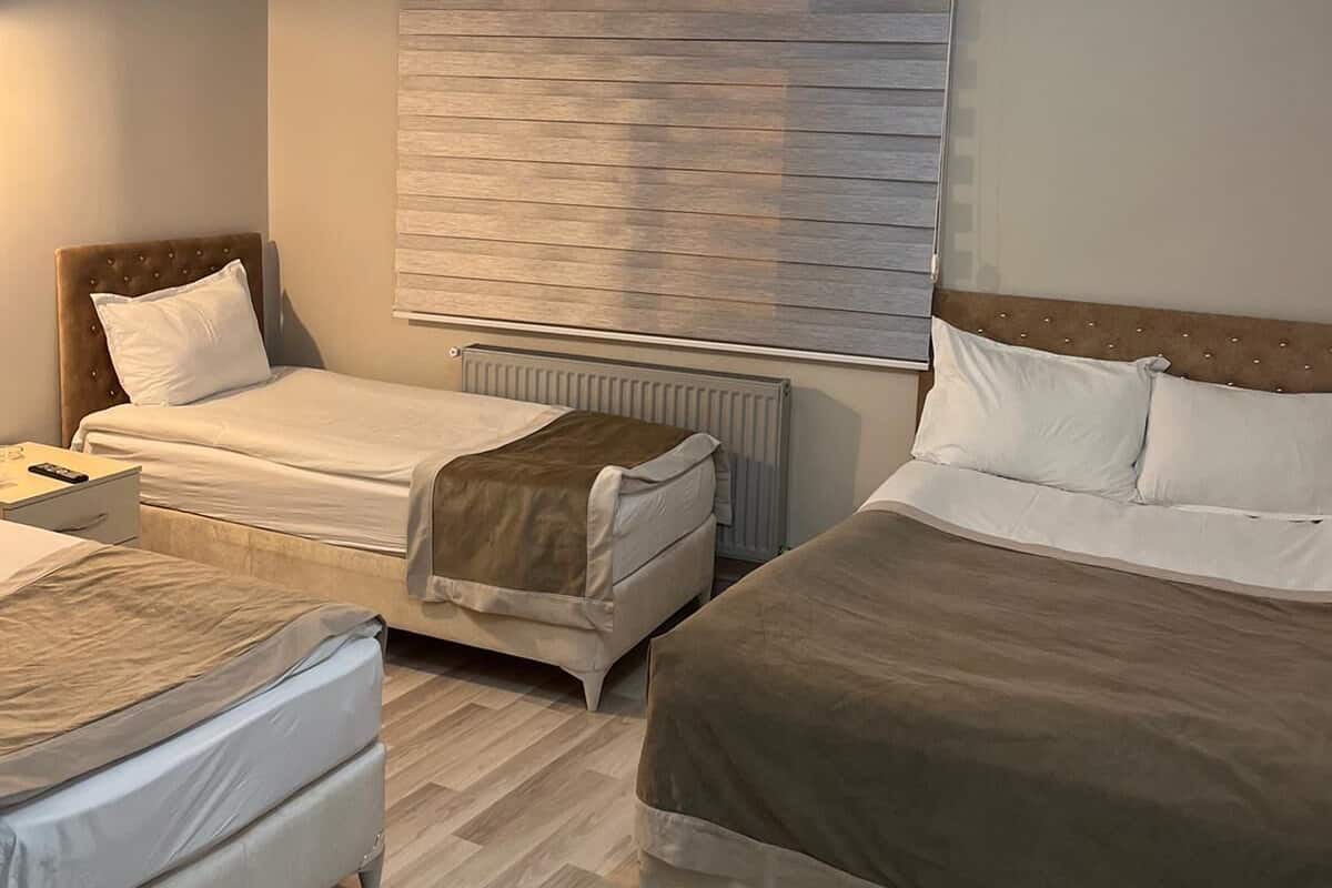 A hotel room with two beds, a wooden floor, a radiator, and a chandelier.