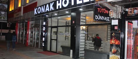 Un hotel con fachada de vidrio, alfombra roja en la entrada y un letrero a la derecha para un restaurante llamado "TUTUN DÜNYASI".