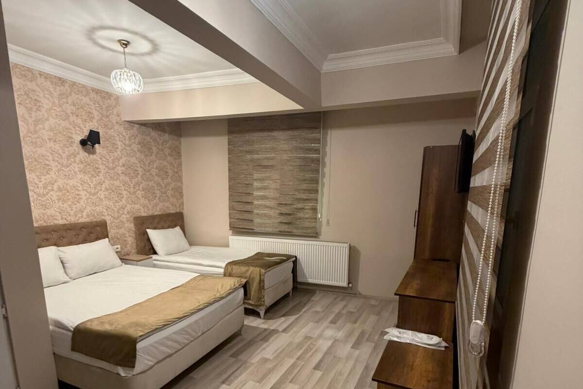 A bedroom with a bed, two bedside tables, a dresser, a radiator, and a chandelier.