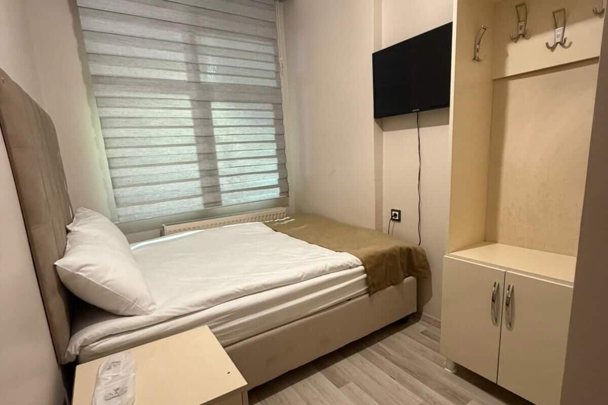 A bedroom with a bed, nightstand, wardrobe, and a TV mounted on the wall.