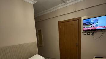 Un dormitorio con una cama, un televisor fijado a la pared y una puerta de madera.