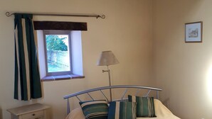 Een slaapkamer met een bed, een raam, een lamp en een klein nachtkastje.