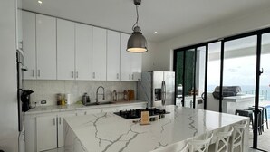 Une cuisine moderne avec des meubles blancs, un îlot en marbre et une grande fenêtre offrant une vue dégagée.