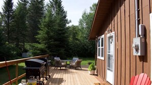 Eine Holzterrasse mit Gartenmöbeln, einem Grill und Propangasflaschen.